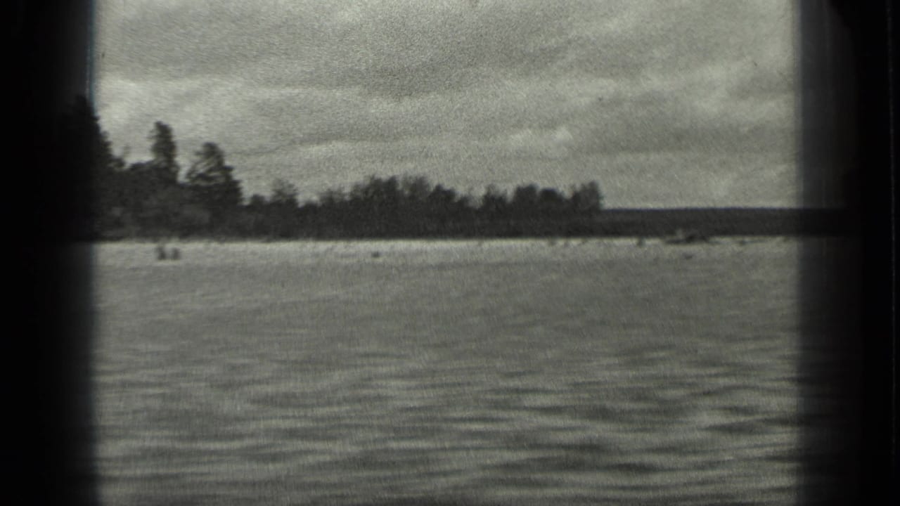 Long Lake, Canada, appears in a grainy 1939 8mm frame with broad water, a dark forested shore, and overcast sky.