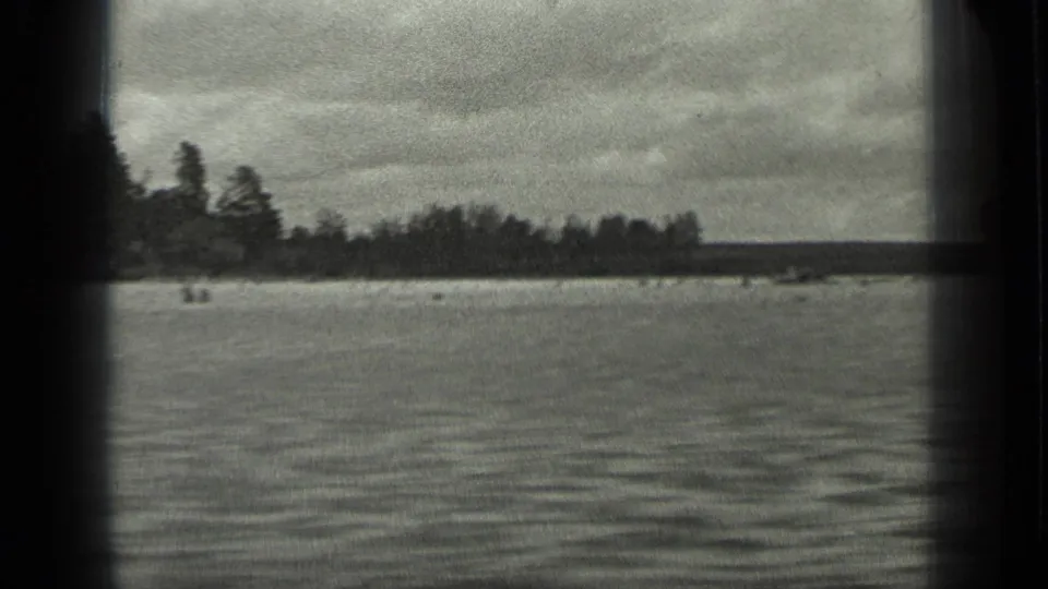 Long Lake, Canada, appears in a grainy 1939 8mm frame with broad water, a dark forested shore, and overcast sky.