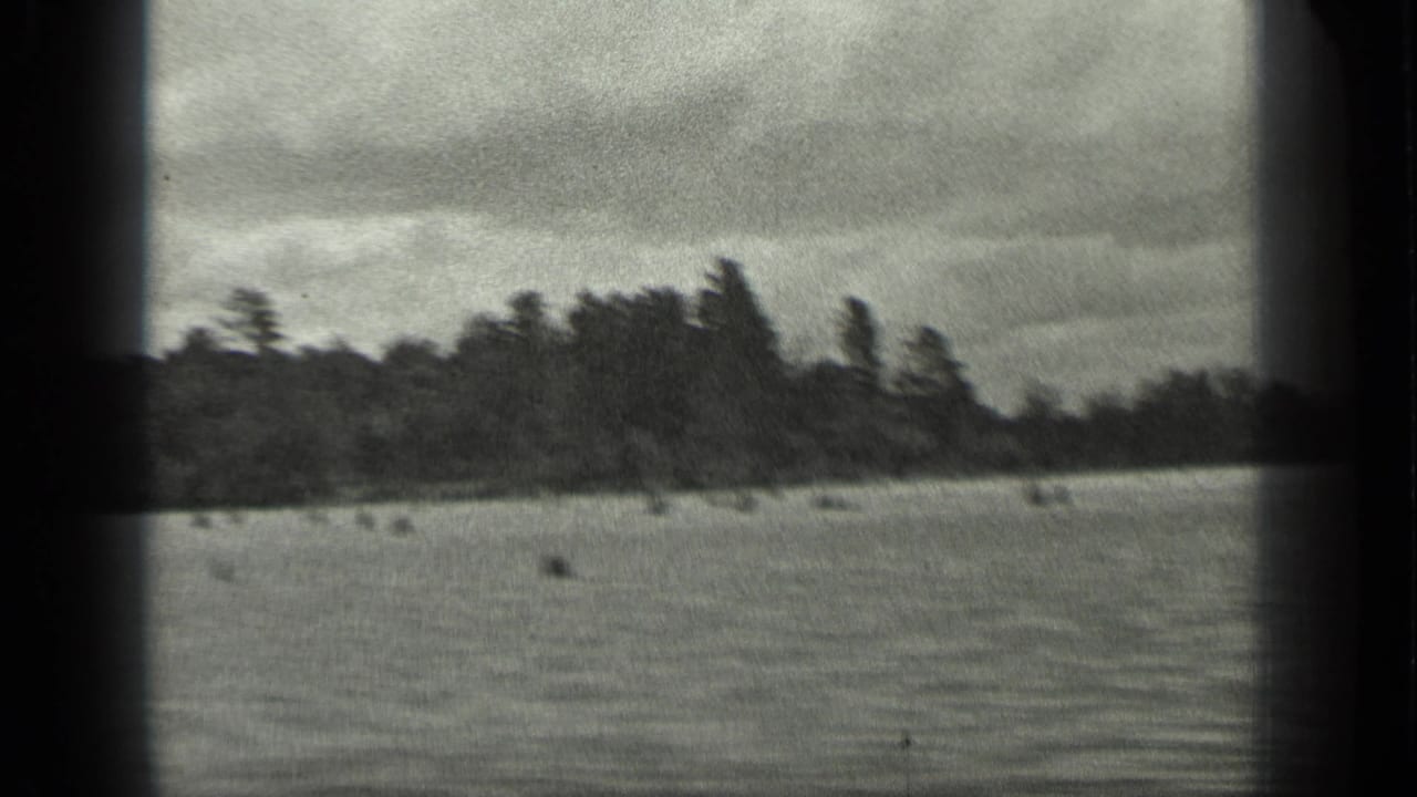 A soft 1939 8mm frame shows Long Lake water in front of a dark tree line, with motion blur and overcast light.