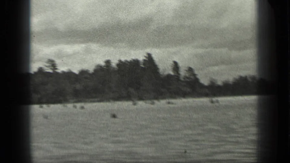 A soft 1939 8mm frame shows Long Lake water in front of a dark tree line, with motion blur and overcast light.
