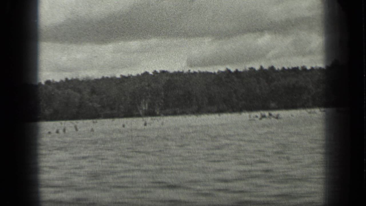 1939 Long Lake, Canada frame with rippled water, low wooded horizon, overcast sky, and a dark vertical gate edge through the scan.