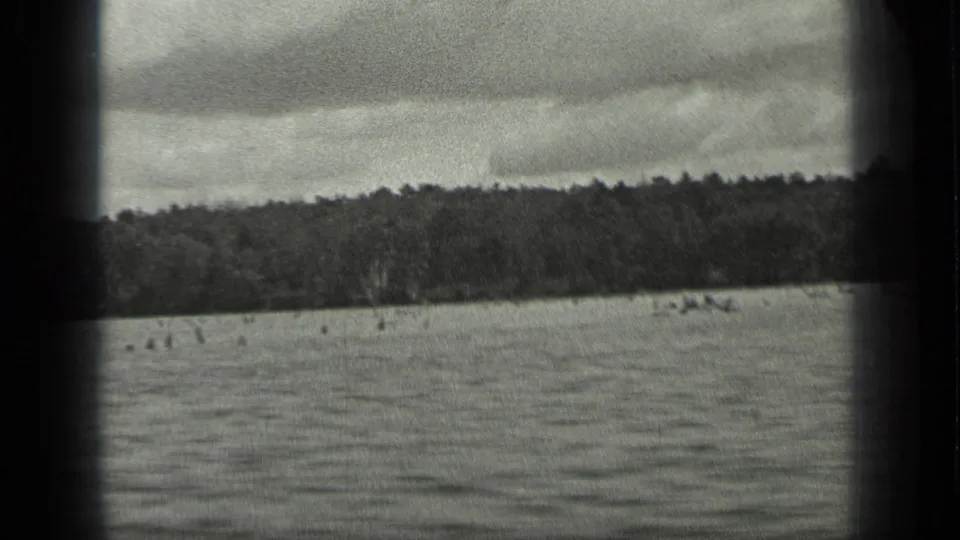 1939 Long Lake, Canada frame with rippled water, low wooded horizon, overcast sky, and a dark vertical gate edge through the scan.