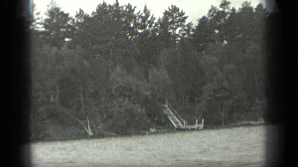 1939 Long Lake, Canada lakeshore view showing water, dense trees, and a small wooden dock or stair structure near the bank.