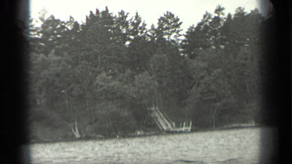 1939 Long Lake, Canada 8mm frame showing the wooded shore, rippled water, and a small wooden dock or ladder set into the bank.