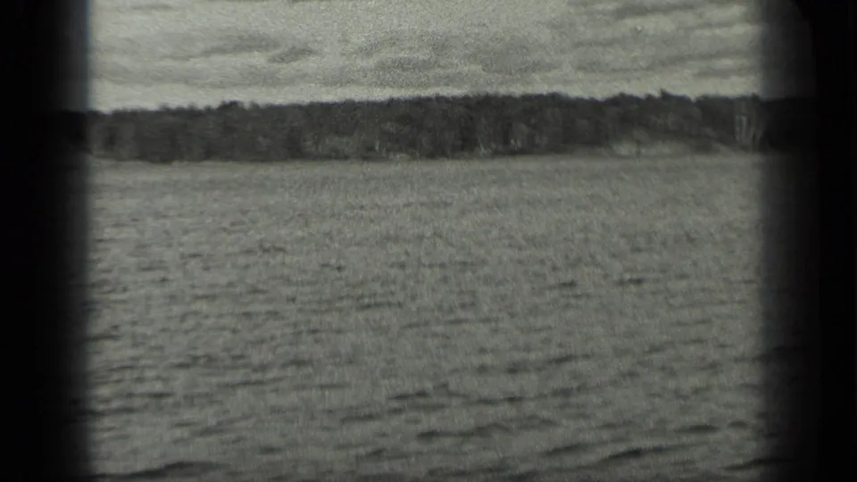 A wide view across Long Lake shows rippled water, a distant tree line, and cloudy sky in black-and-white 8mm footage.