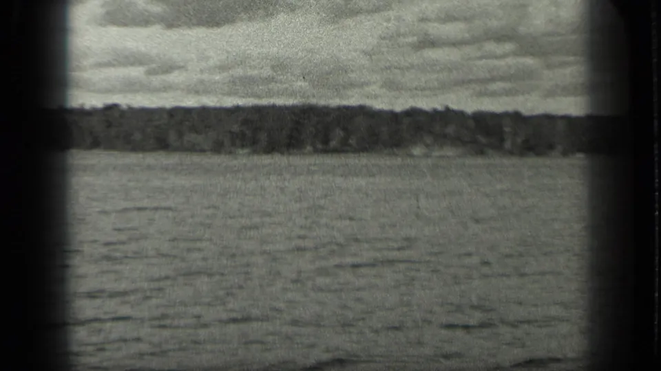 A wide black-and-white 8mm view of Long Lake shows calm water, a forested horizon, and cloud cover.