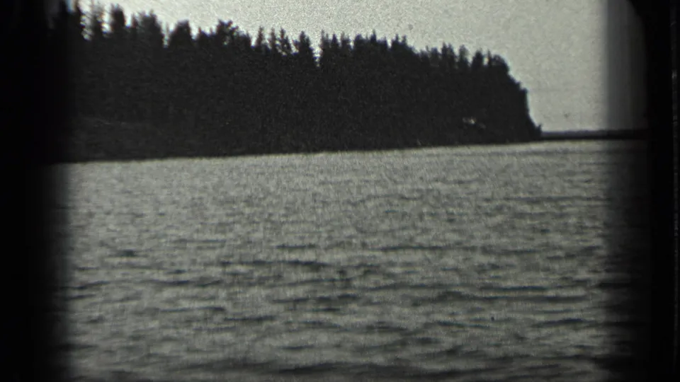 1939 Long Lake, Canada home-movie frame showing a dark wooded point, rippled water, pale sky, and rounded film-frame edges.