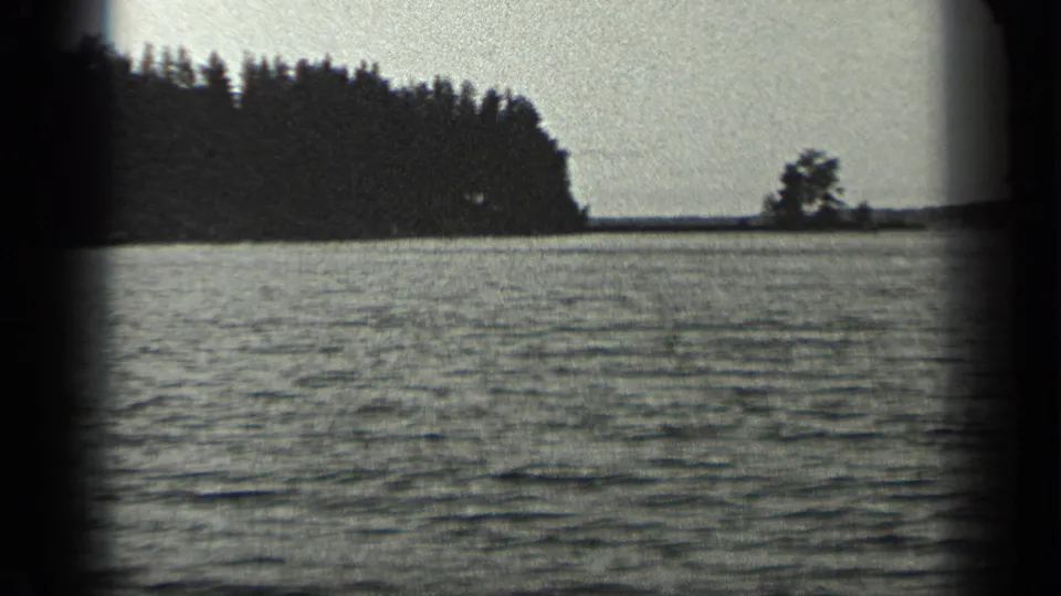 1939 Long Lake, Canada frame showing rippled water, a dark forested shoreline, and a small tree silhouette near the far right horizon.