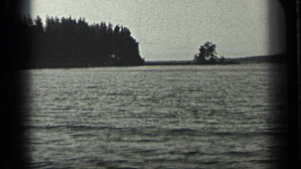 1939 8mm home-movie frame of Long Lake, Canada, showing rippled water, distant wooded shore, and bright sky.