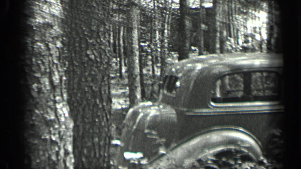 1939 Long Lake, Canada 8mm frame showing a rounded vintage automobile parked beside tall trees in the woods.