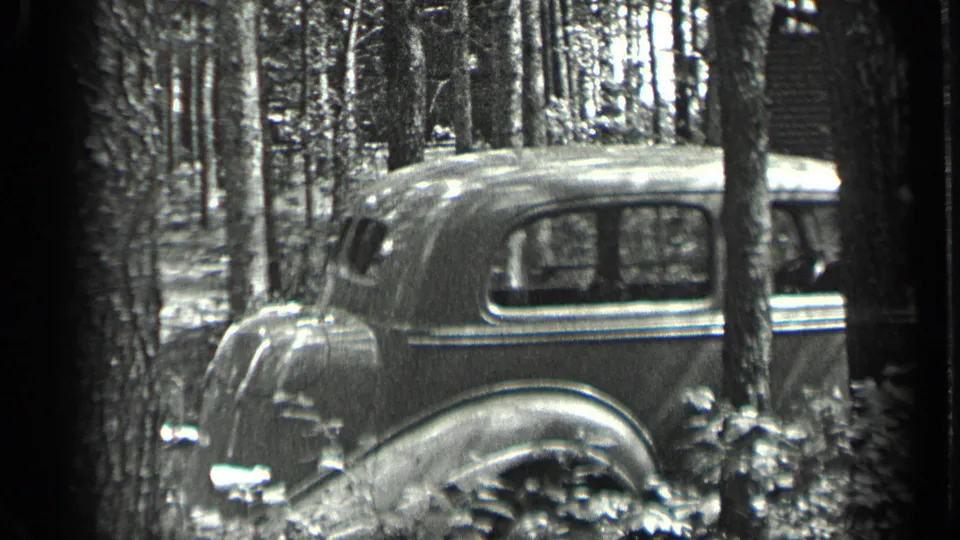 A late-1930s style car appears parked in a Long Lake, Canada forest in black-and-white 8mm footage.