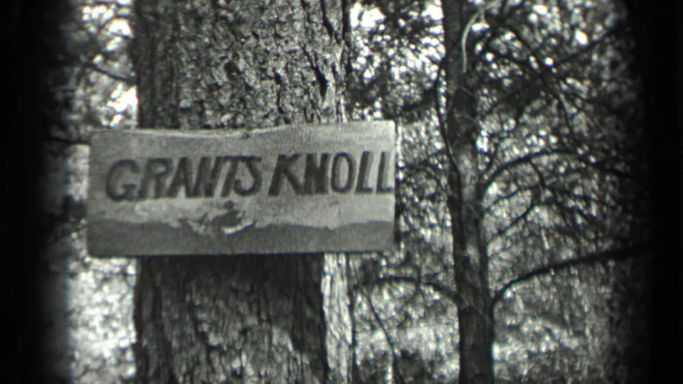 The GRANTS KNOLL marker fills the frame against a large tree trunk in grainy black-and-white 8mm footage.
