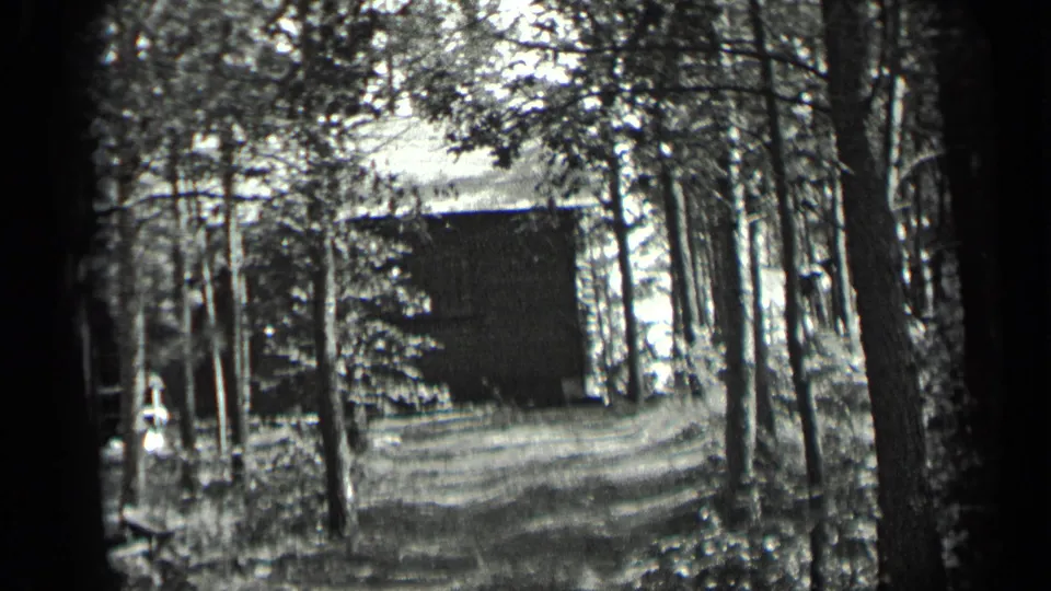 Black-and-white 8mm frame from Long Lake, Canada showing a cabin framed by trees and a shaded driveway.