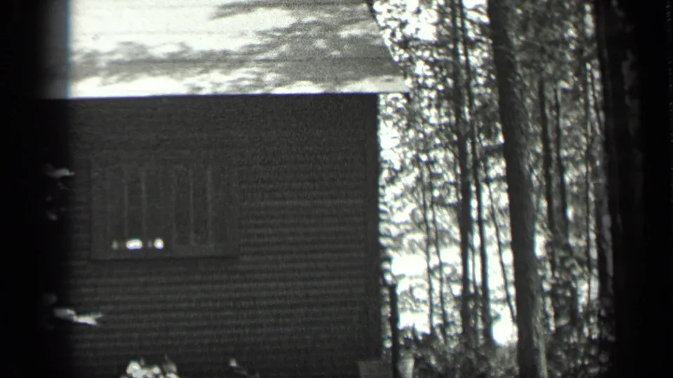 Closer 1939 home-movie view of the cabin exterior, with a low roofline, small windows, and surrounding trees.