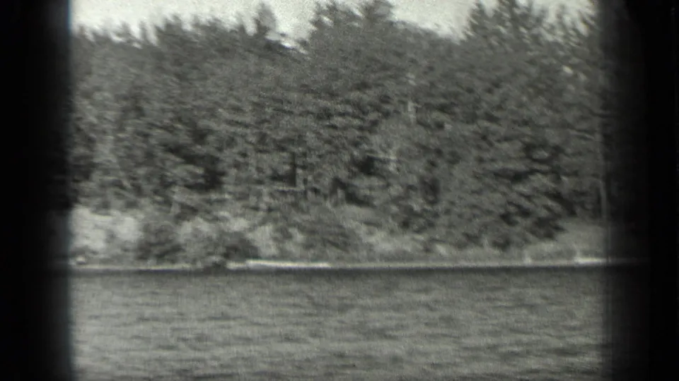 1939 home-movie frame from Long Lake, Canada, with rippled water below a continuous wooded shoreline.