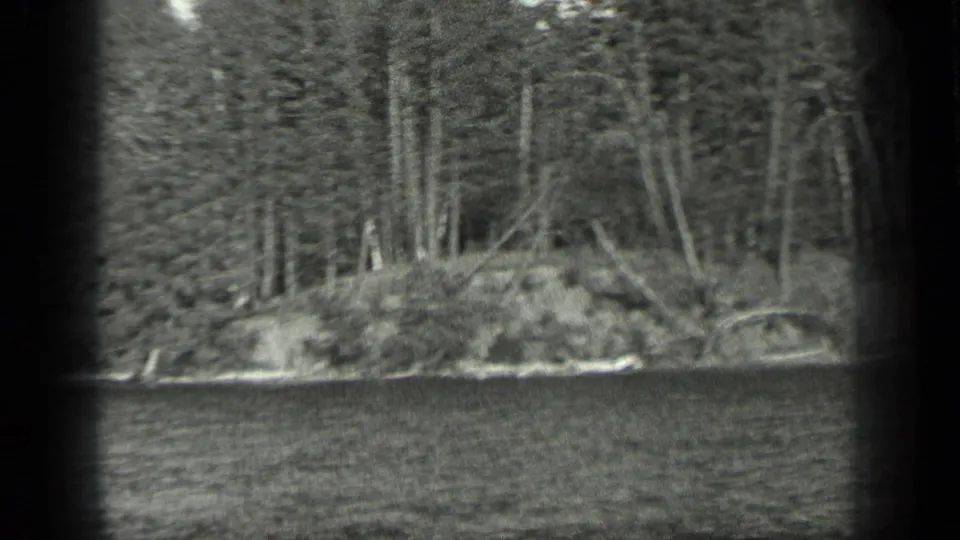 1939 Long Lake, Canada home-movie view of a wooded shoreline across rippled water, framed by dark film-gate edges.