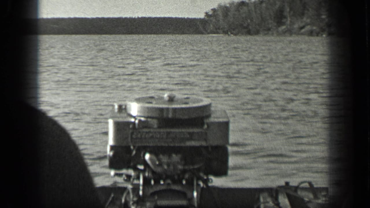 Outboard motor mounted on a boat, seen from close range on Long Lake, Canada, with water and distant trees beyond.