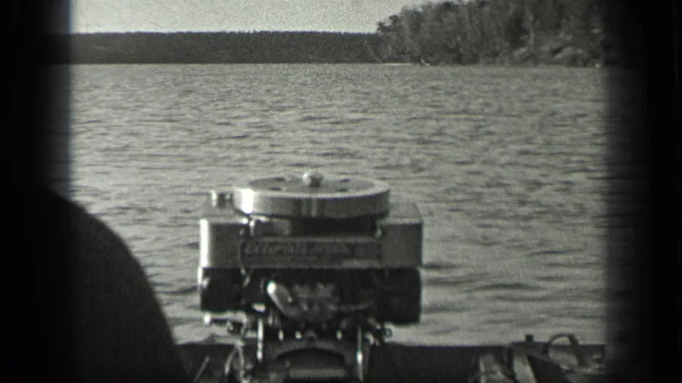 Outboard motor mounted on a boat, seen from close range on Long Lake, Canada, with water and distant trees beyond.