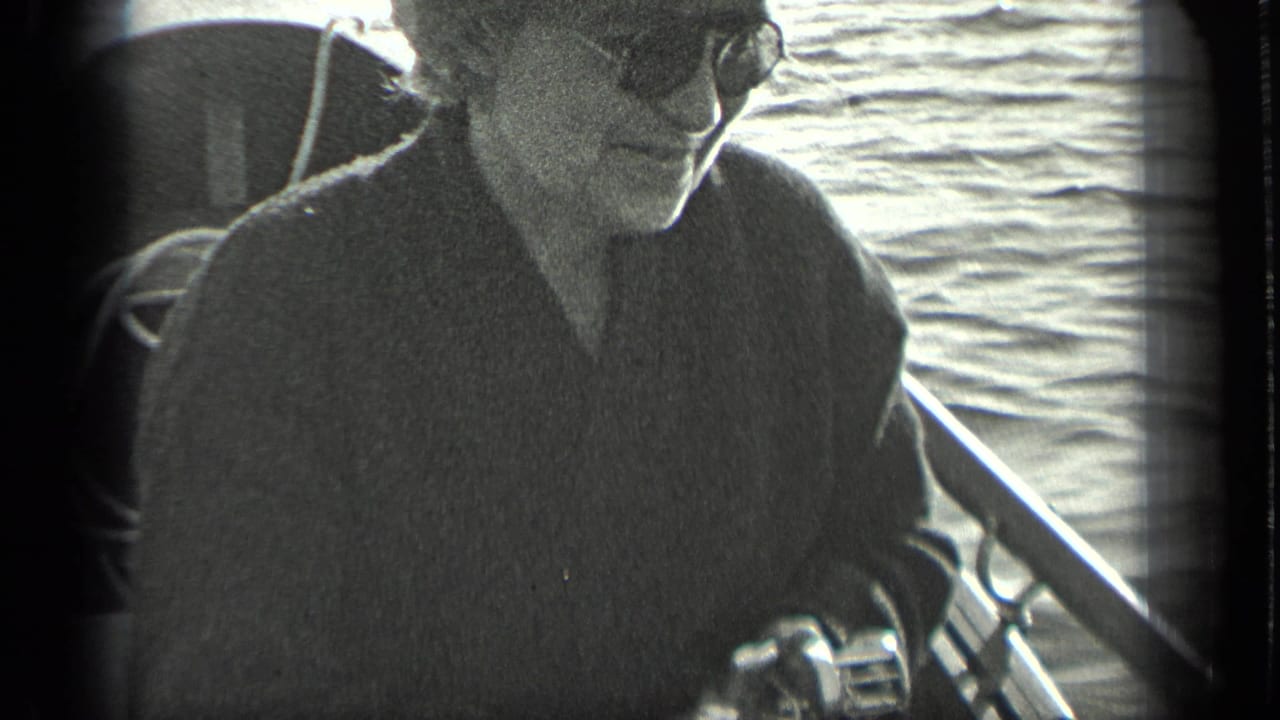 Woman in sunglasses sits on a boat beside fishing gear and lake water.