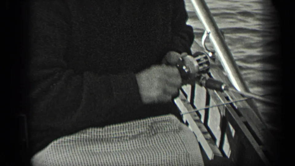 1939 Long Lake home-movie frame showing a close view of an adult handling a fishing reel and rod beside the boat railing.