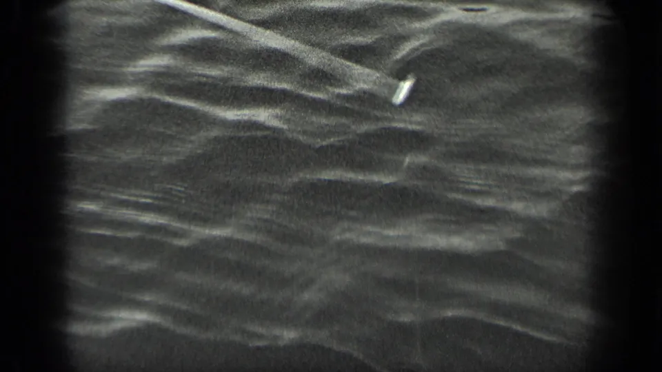 Black-and-white 8mm frame from Long Lake, Canada showing rippled water and a small bright fishing line or lure.