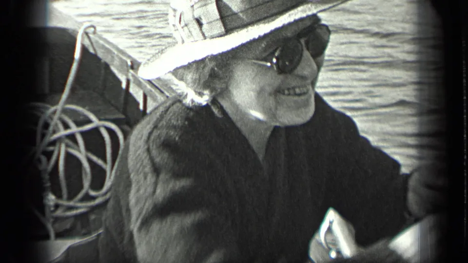 Older woman in a brimmed hat and sunglasses sits in a boat on Long Lake, Canada, with rope and water visible behind her.