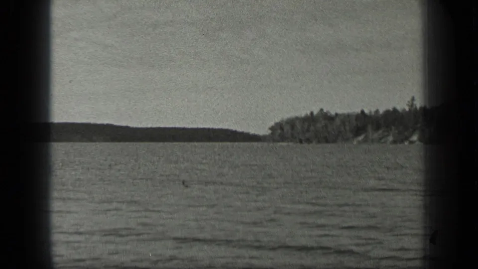 Long Lake, Canada shoreline appears across rippled water in a grainy 1939 black-and-white home-movie frame.