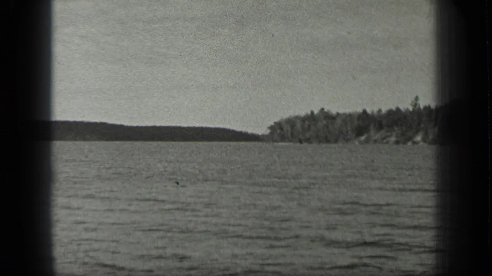 Black-and-white 8mm view of Long Lake, Canada, showing gentle waves and a wooded shore under a plain sky.