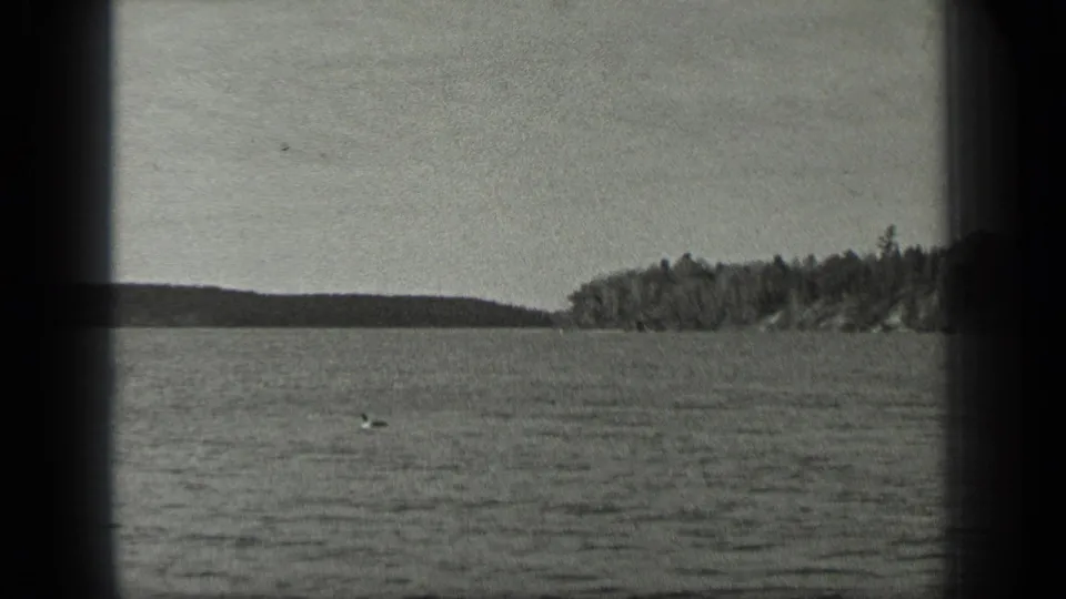 1939 Long Lake, Canada home-movie frame showing rippled water, a distant tree-lined shore, pale sky, and dark 8mm frame borders.