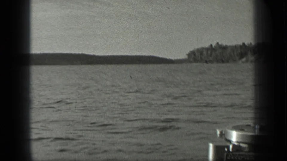 1939 Long Lake, Canada frame showing rippled water, distant trees, and partial camera or boat hardware entering the lower right edge.