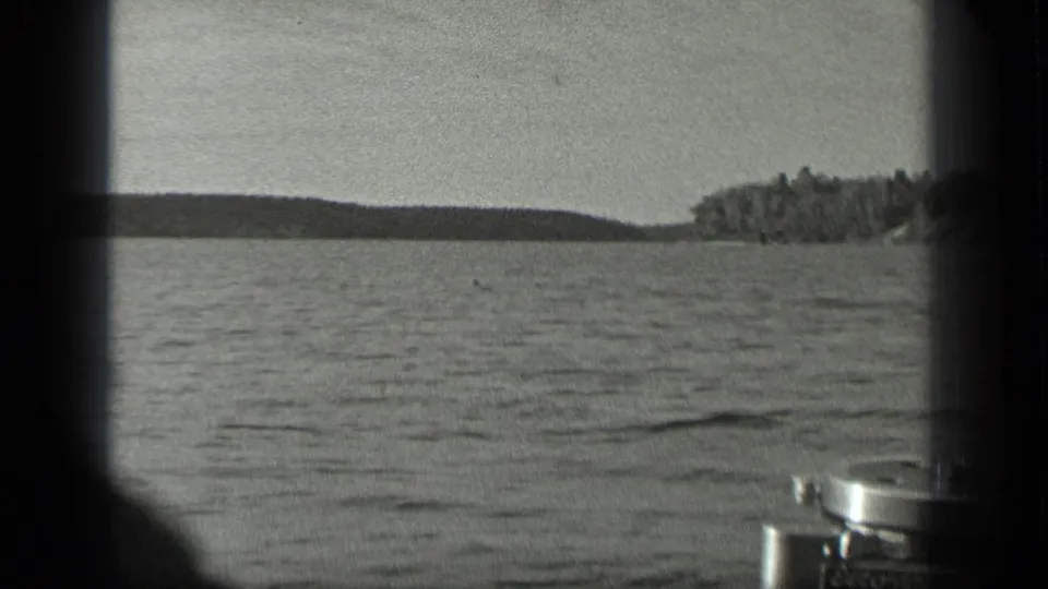 1939 Long Lake, Canada home-movie frame showing open water, distant trees, and part of a small boat or motor at the edge.