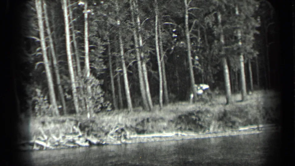 1939 Long Lake home-movie frame showing wooded shoreline, rippled water, and a distant human figure or small craft near the trees.