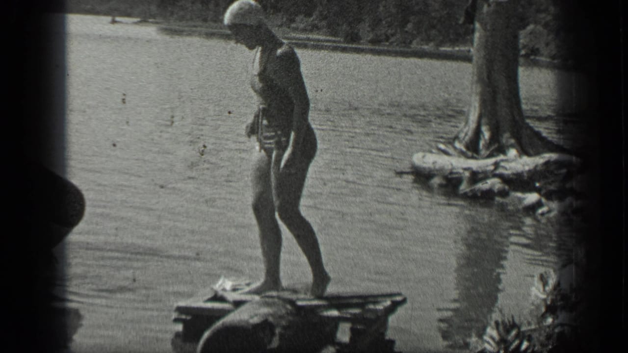 Woman in swim cap stands on a wooden dock beside lake water.