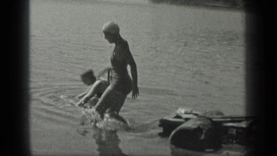 At Long Lake, Canada in 1939, one woman steps off the dock into the lake as another person swims close to shore.