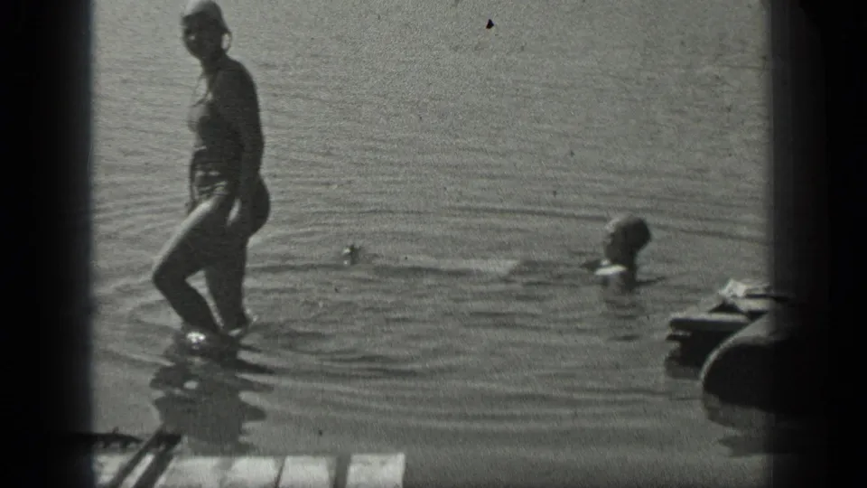 At Long Lake, Canada in 1939, one woman stands near the shore while another swimmer moves across the lake surface.