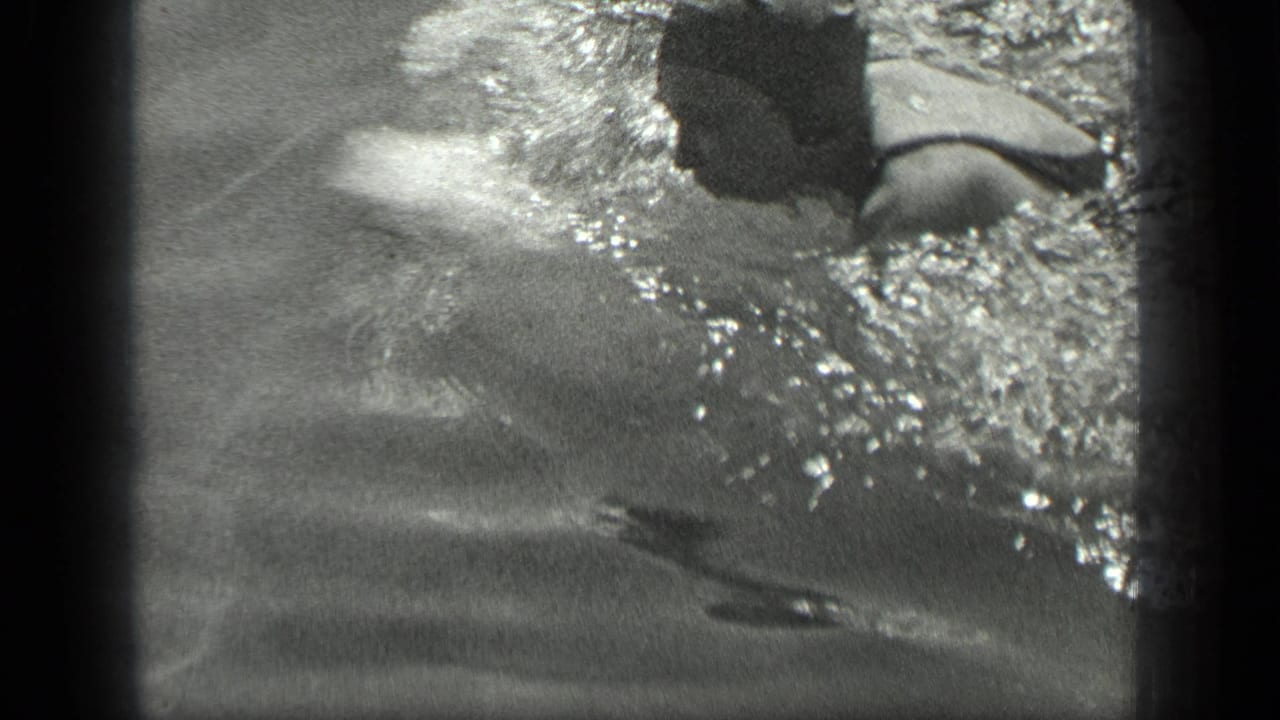 Capped swimmer moving through dark lake water with splashes around the head and shoulders.