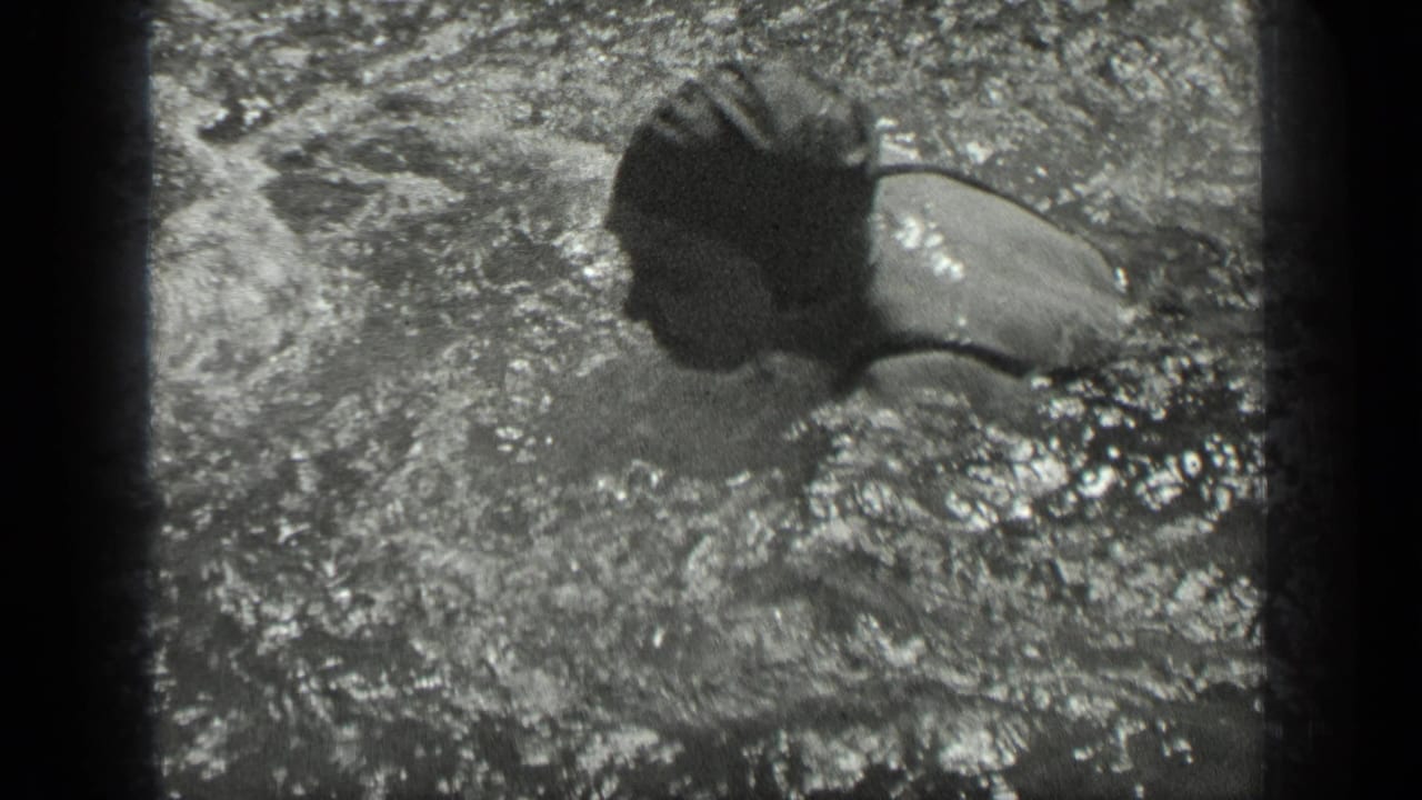 A capped swimmer crosses the frame in Long Lake, Canada, with active splashing visible in the black-and-white 8mm image.
