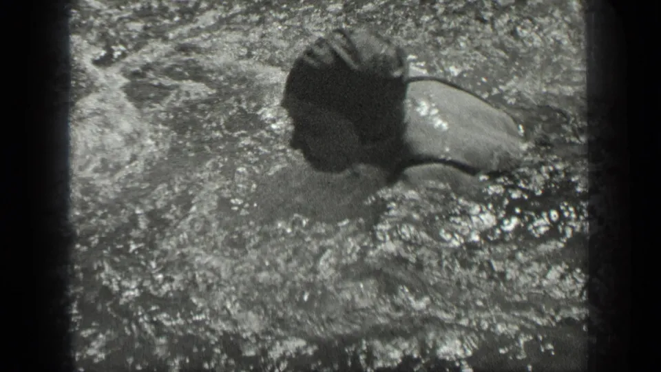 A capped swimmer crosses the frame in Long Lake, Canada, with active splashing visible in the black-and-white 8mm image.