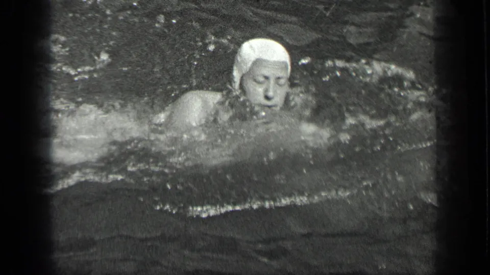 A swimmer in a white cap faces the camera during a stroke in 1939 Long Lake, Canada home-movie footage.