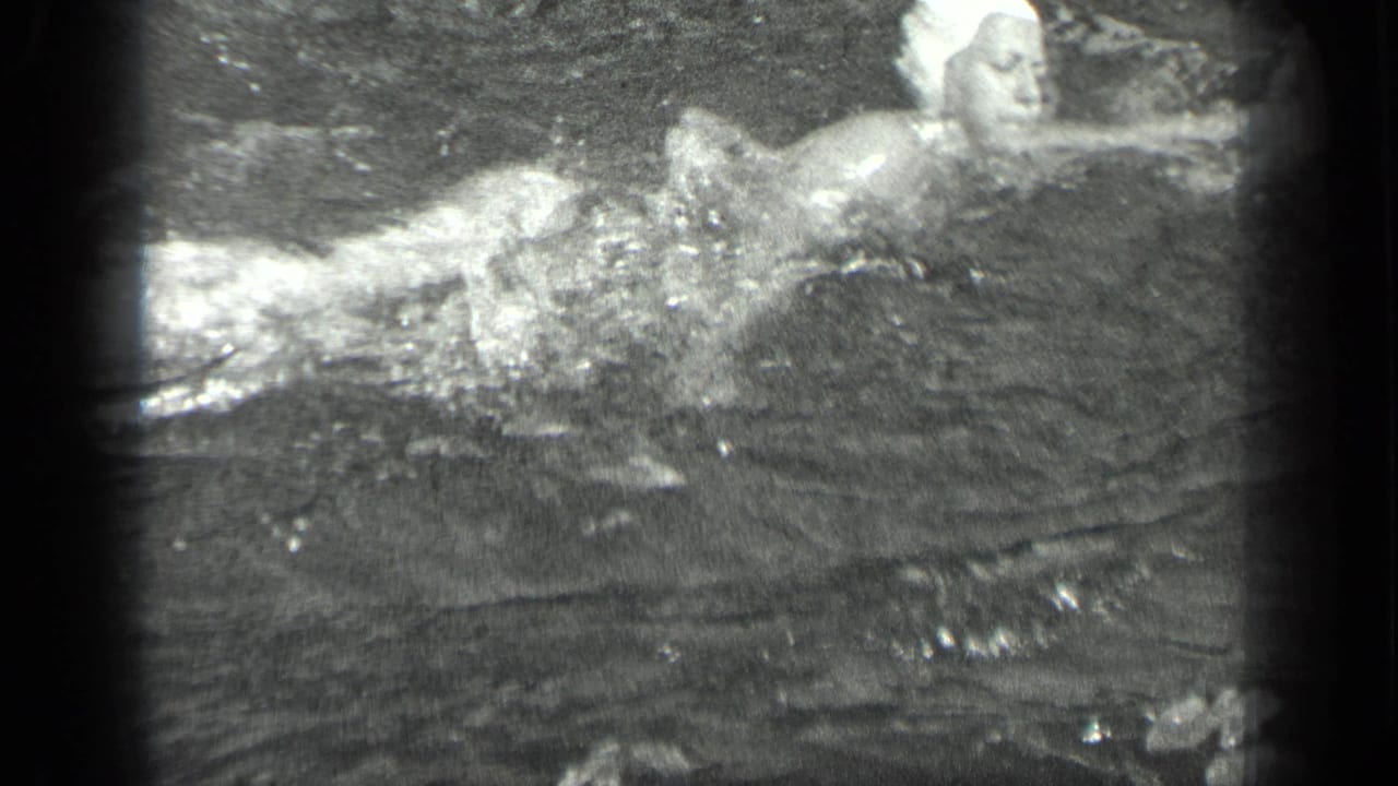 Woman in a white swim cap swims through rippling lake water.