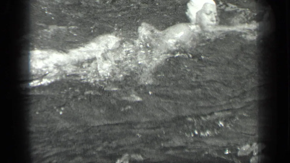 1939 Long Lake, Canada footage shows a woman in a white swim cap and light swimsuit swimming across rippling water.