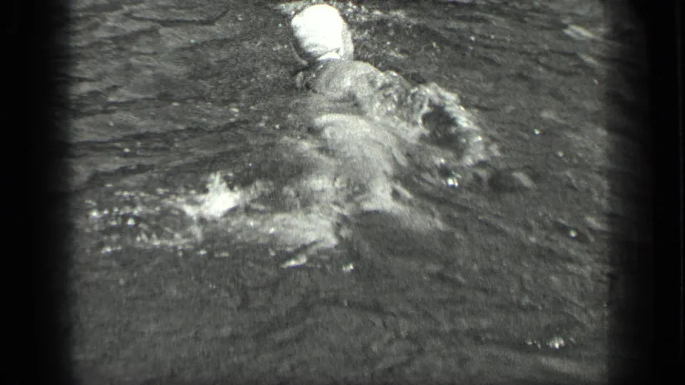 The swimmer is seen from behind in 1939 Long Lake footage, with her white cap and shoulders visible amid churning water.