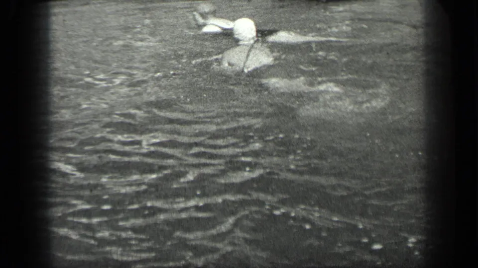 1939 home-movie frame of a capped swimmer partly submerged in Long Lake water.