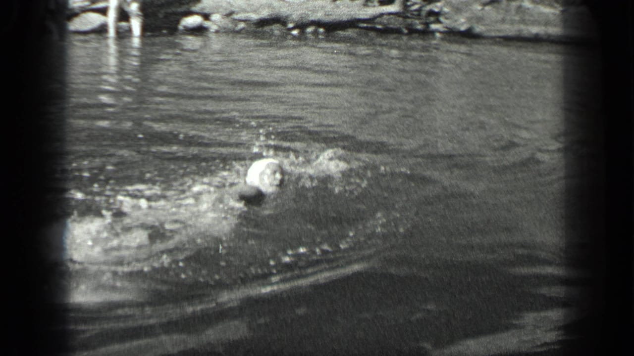 A swimmer in a light cap creates splashes while moving through the Long Lake water in the 1939 home movie.