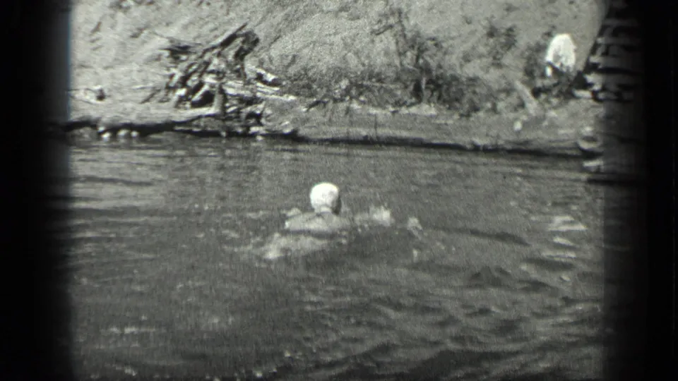 The swimmer is seen from behind or at an angle in the water below the natural Long Lake shoreline.