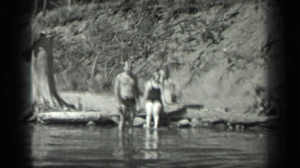 1939 Long Lake, Canada home-movie frame showing three people at the water's edge with trees and calm lake reflections.