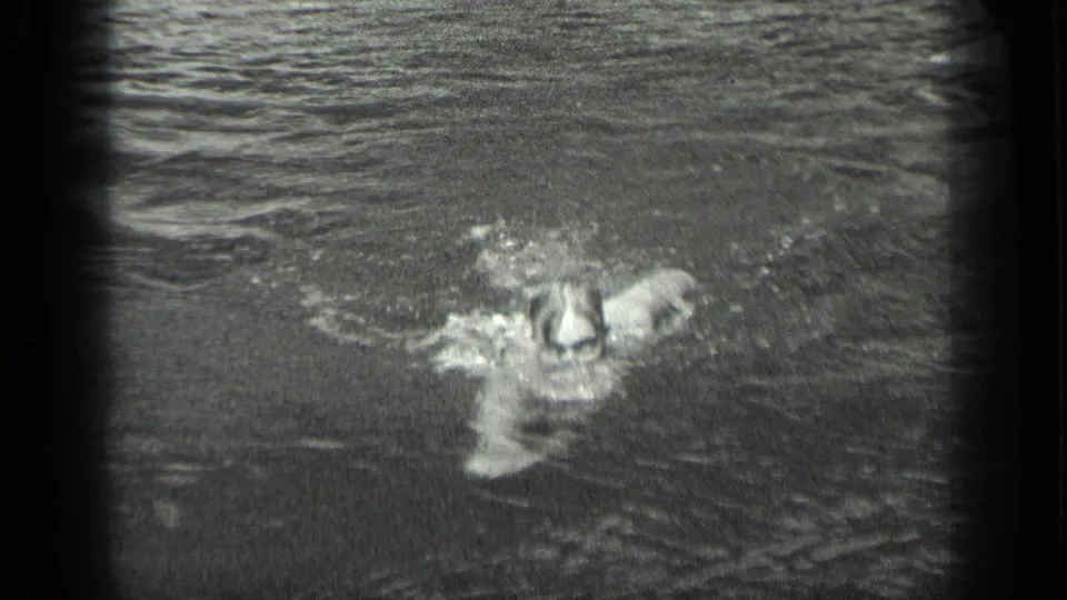 In 1939 Long Lake home-movie footage, a woman swims toward the camera through calm water with soft ripples and splashes.