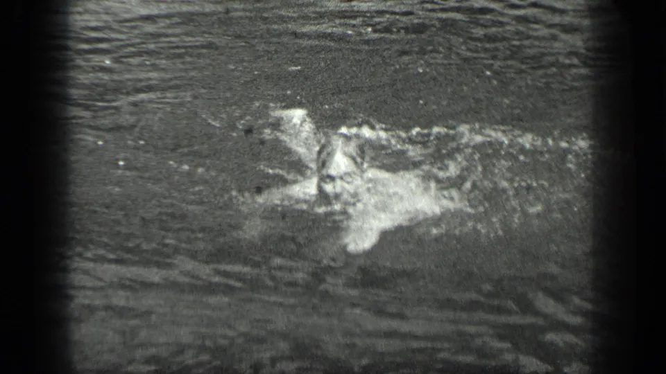A 1939 home-movie frame shows the swimmer partly submerged during a stroke, surrounded by ripples and bright water highlights.