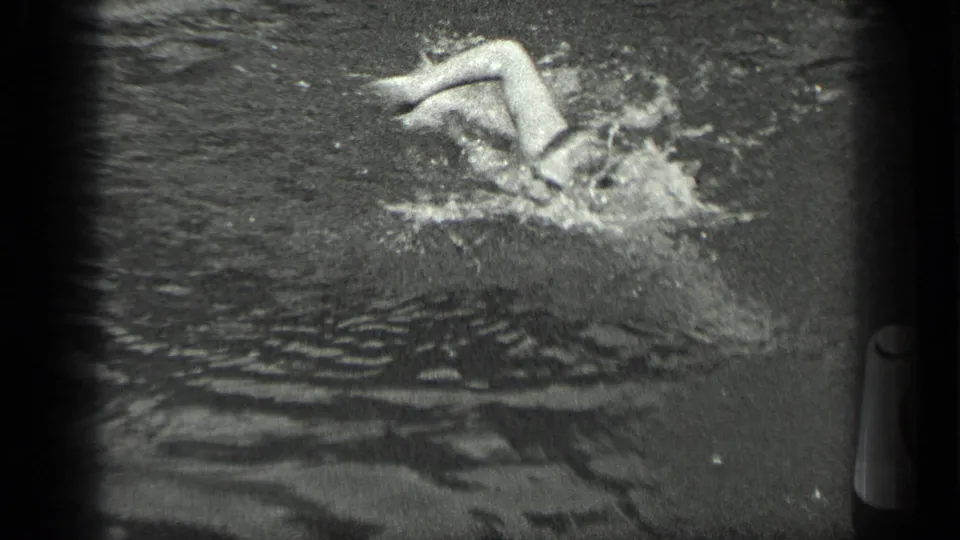 The swimmer kicks with both legs above the water in the 1939 Long Lake footage, creating splashes around her upper body.