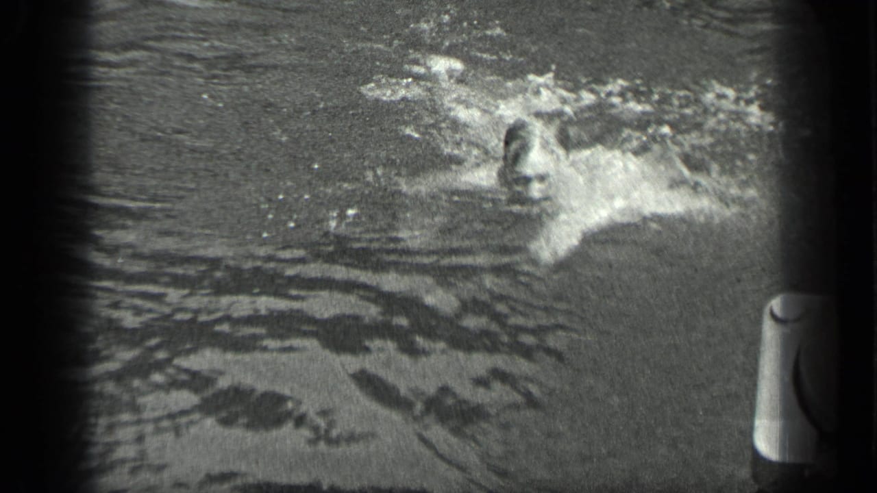 A swimmer moves through Long Lake water in 1939 home-movie footage, creating bright splashes near a dock or boat edge.